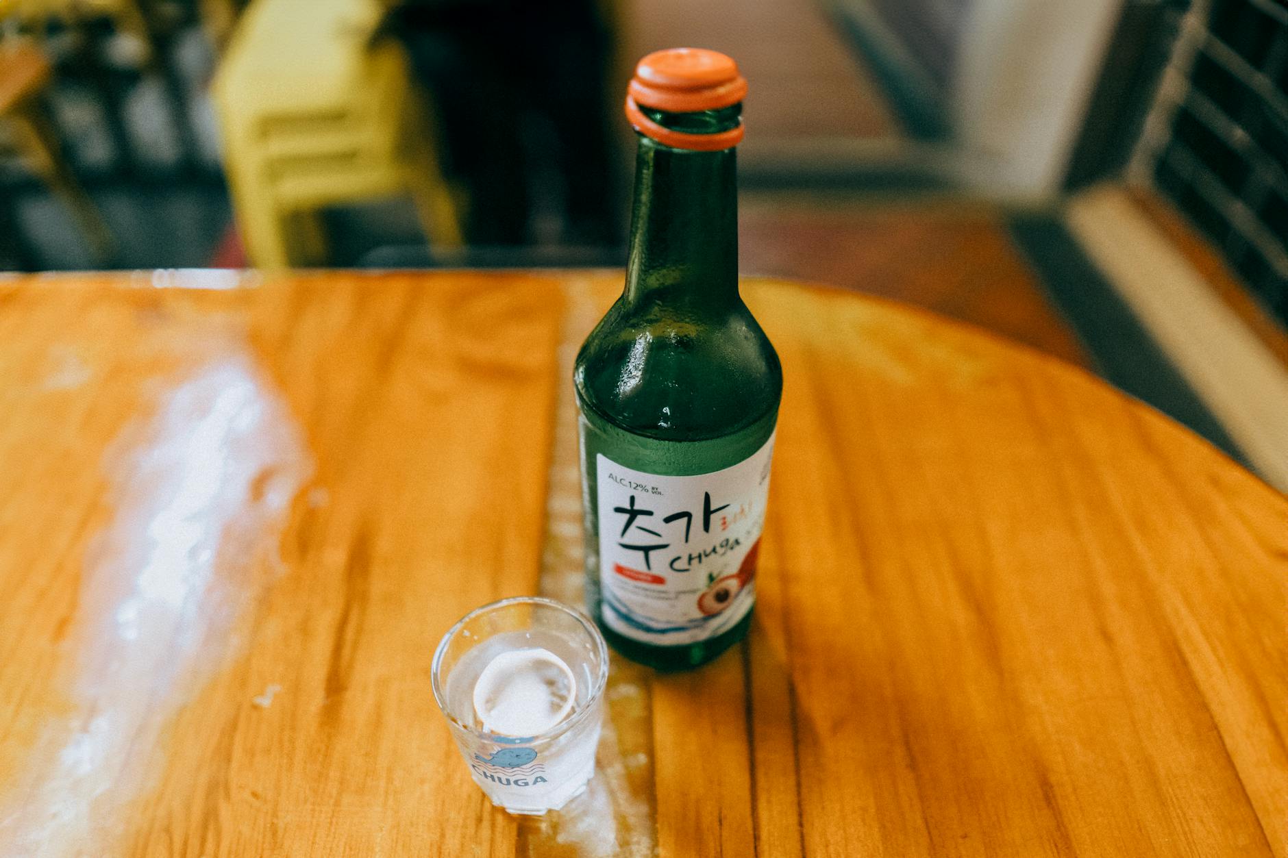 Soju bottle and shot glass on a wooden table at a Korean pojangmacha outdoor night drinking setting