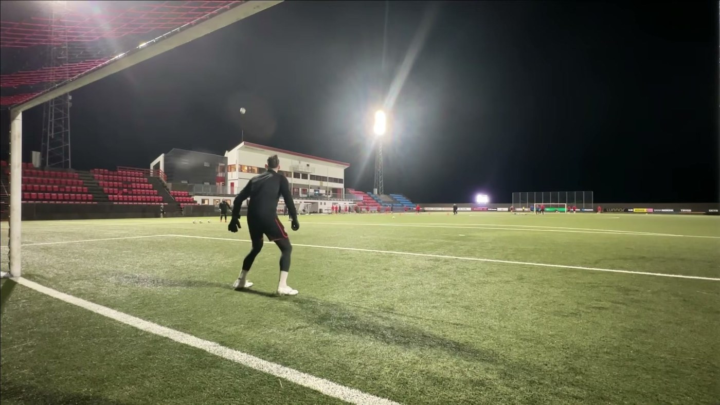 Goalkeeper training alone under a floodlight at night on an empty pitch