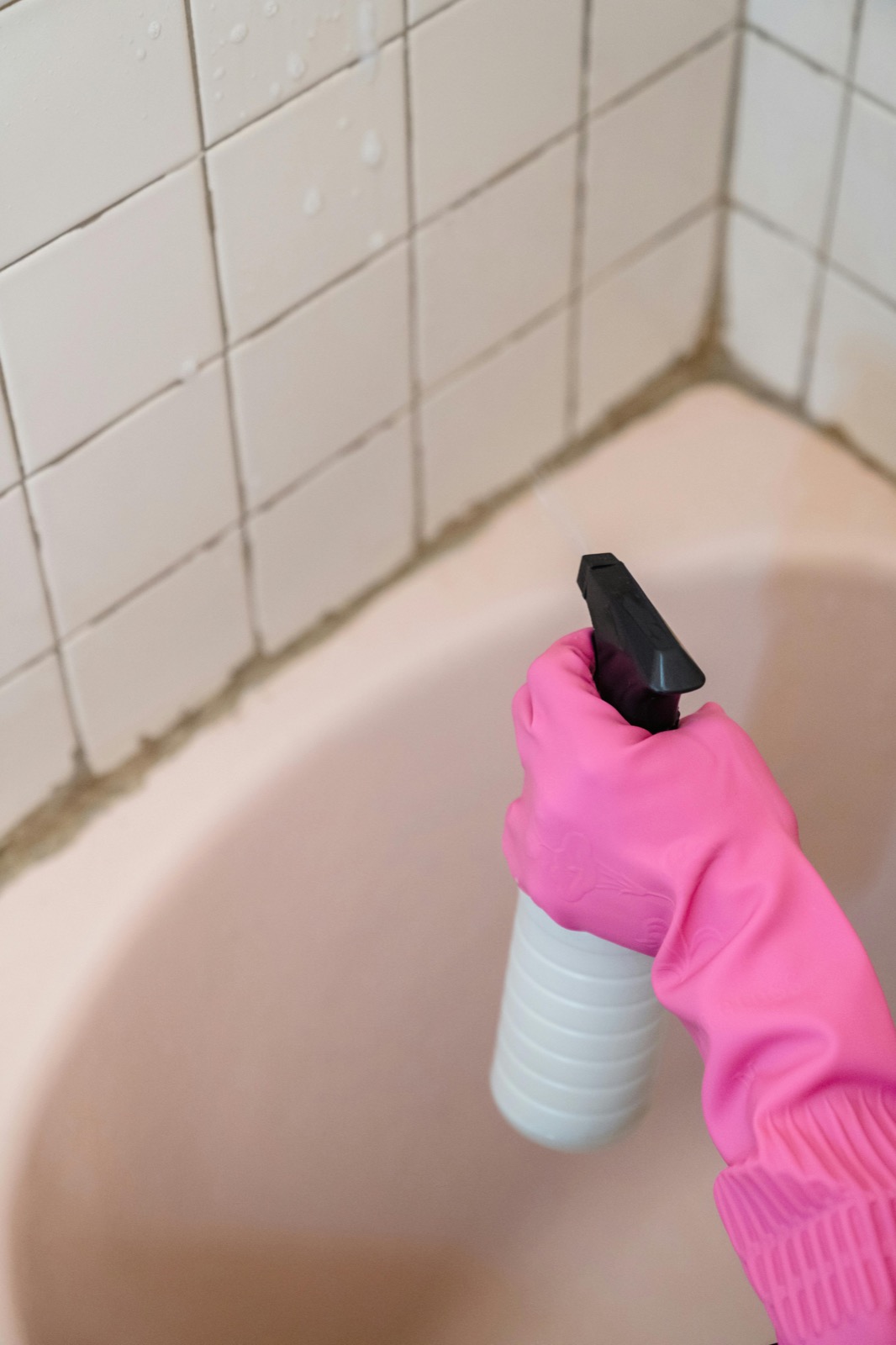 Gloved hand spraying bathroom tiles with visible grout lines