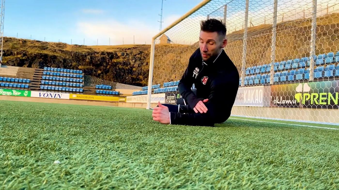 Goalkeeper sitting on the grass gliding sideways onto a ball with both hands, no height, no impact