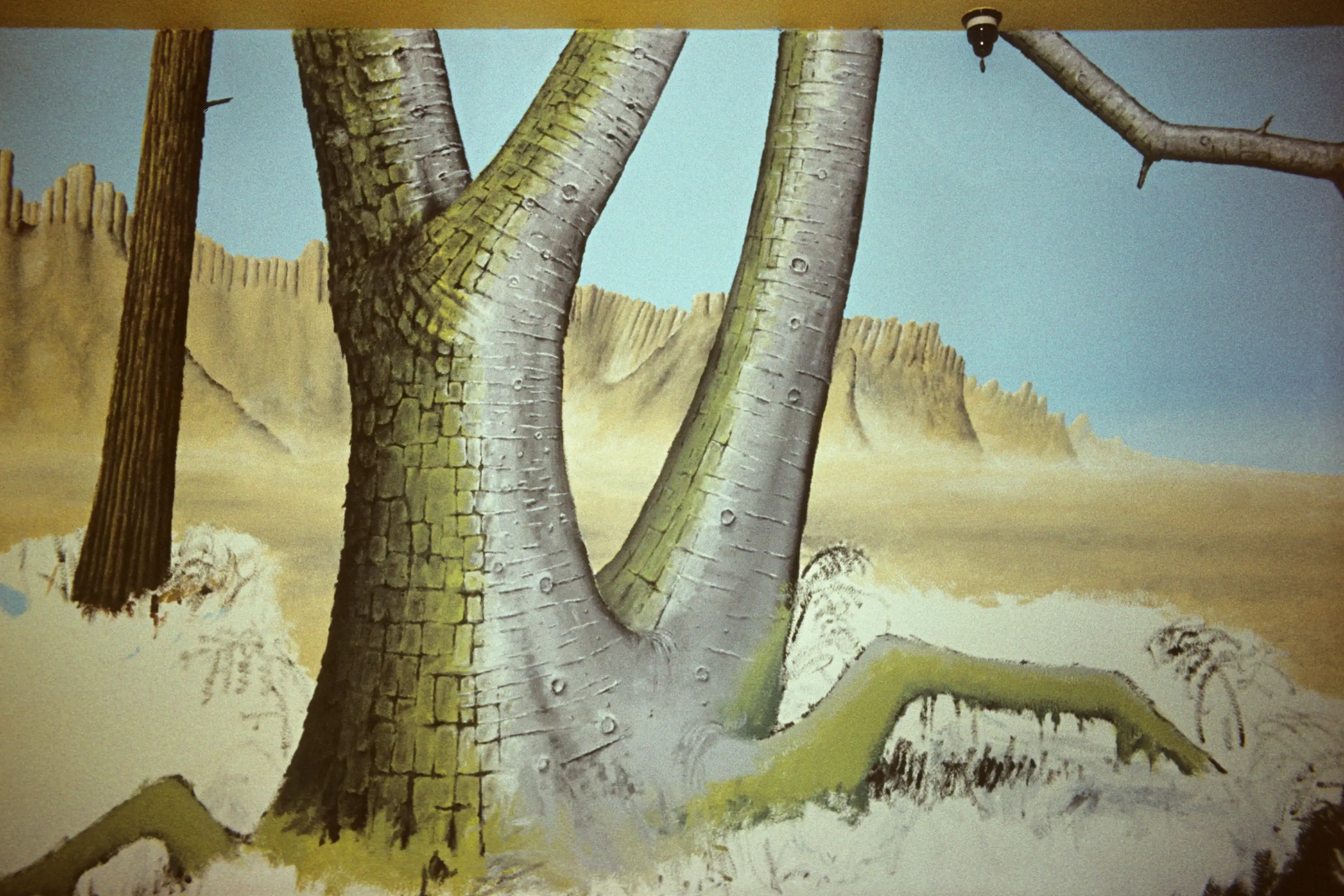 An earlier, incomplete attempt at a mural, with a plane tree to the left, and a desert and mountain ridges beyond.