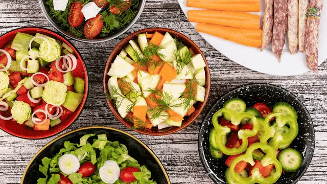 Healthy Salad Recipes Top-down view of various fresh salad bowls with colorful vegetables and herbs on a rustic wooden table.