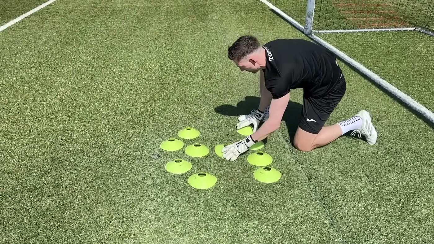 Goalkeeper kneeling on the pitch setting out training cones before a session