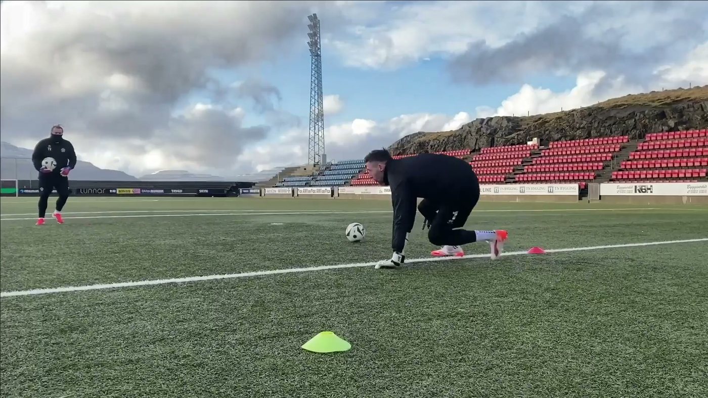 Goalkeeper kneeling on the pitch setting out cones before a session