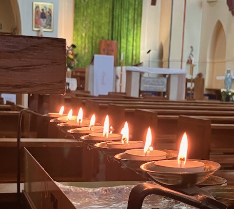 Lit candles glowing in church pews before an altar with green curtains and religious artwork