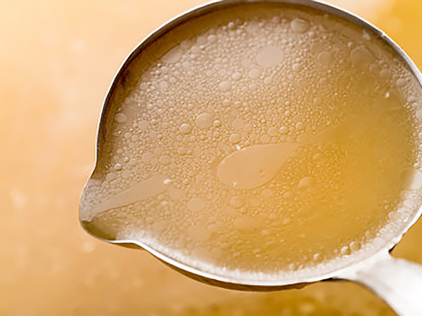 Golden chicken stock in glass vessel showing perfect clarity and color