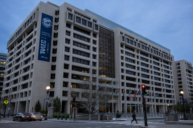 The exterior of the International Monetary Fund headquarters in Washington with flags, editorial news photography at dusk