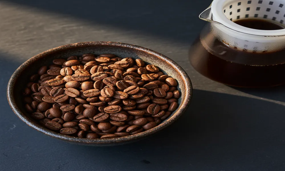 Grãos grandes de Pacamara em bowl de cerâmica escura com jarra Hario Mizudashi ao fundo