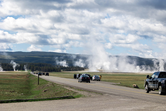 Yellowstone geyser with vehicles in the distance