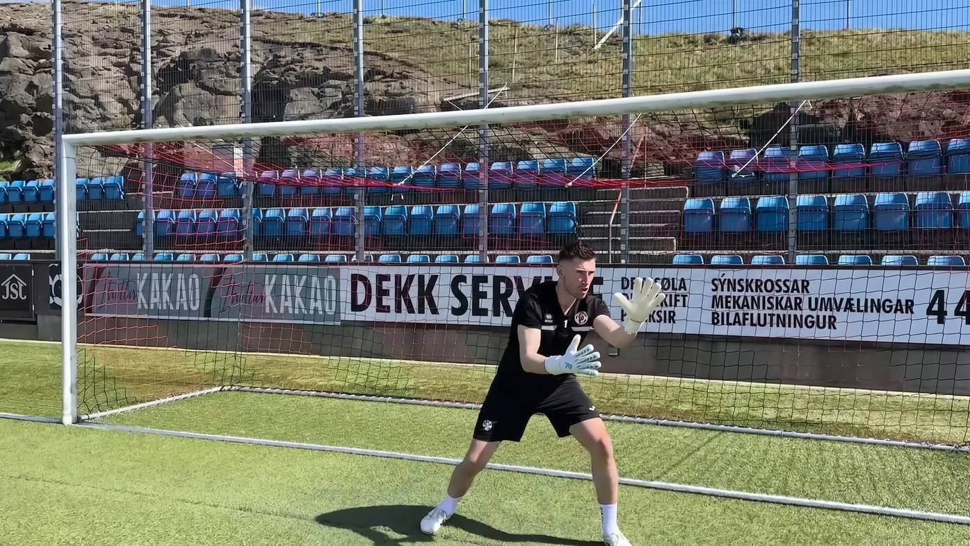 Goalkeeper in his goal pointing firmly with one arm to direct a defender
