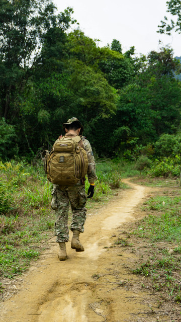 Army infantryman rucking solo on mountain trail with tactical pack and proper upright posture