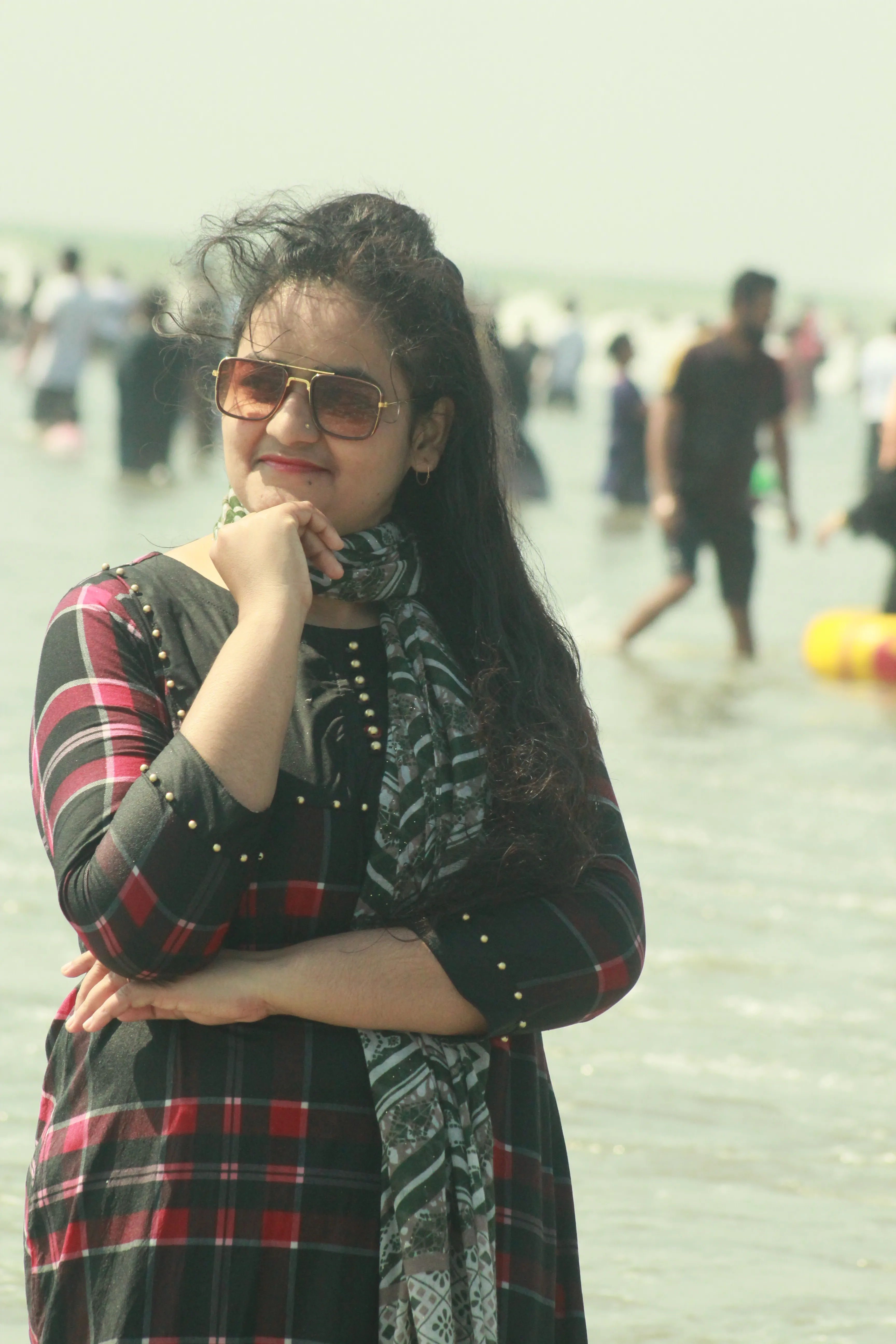 elizabeth A young woman wearing a black and red plaid dress and sunglasses posing thoughtfully on a sunny beach.