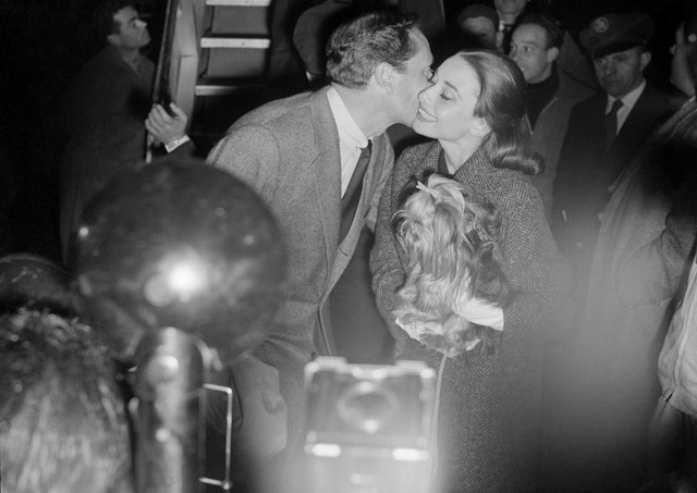 Joyful reunion--Rome, Italy--Actor Mel Ferrer kisses his wife, actress Audrey Hepburn, upon his arrival from Paris last Friday. Miss Hepburn carries pet dog (complete with hair ribbon) during the Ciampino Airport reunion. She is making a movie in the Eternal City.