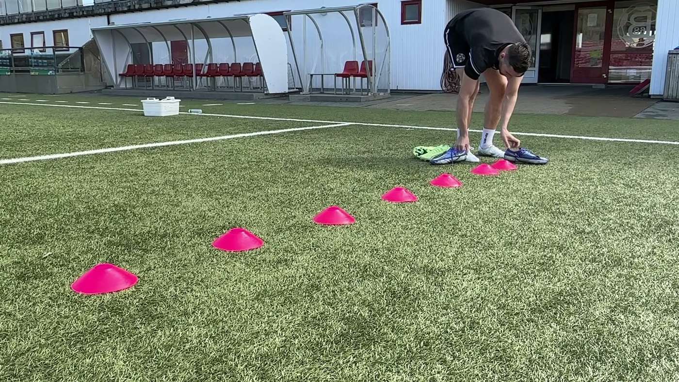 Goalkeeper bending down to set out a line of cones on the pitch before a session