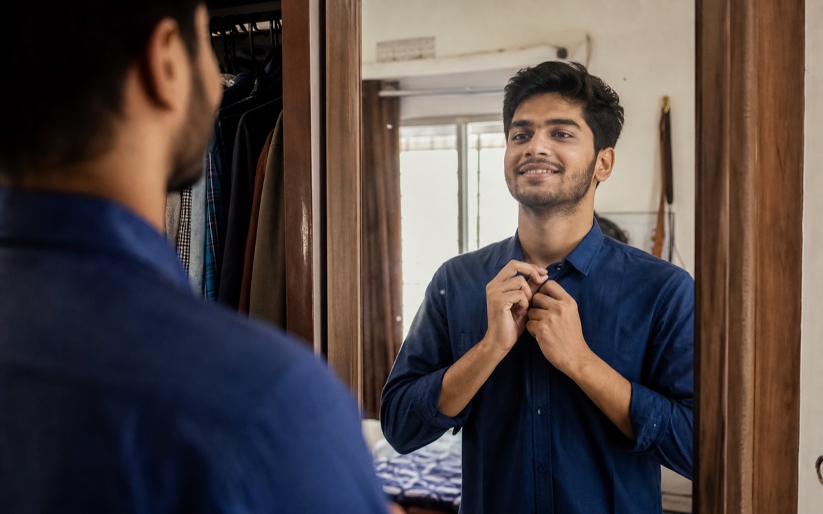 A young Indian man feeling more confident while dressing in front of a mirror