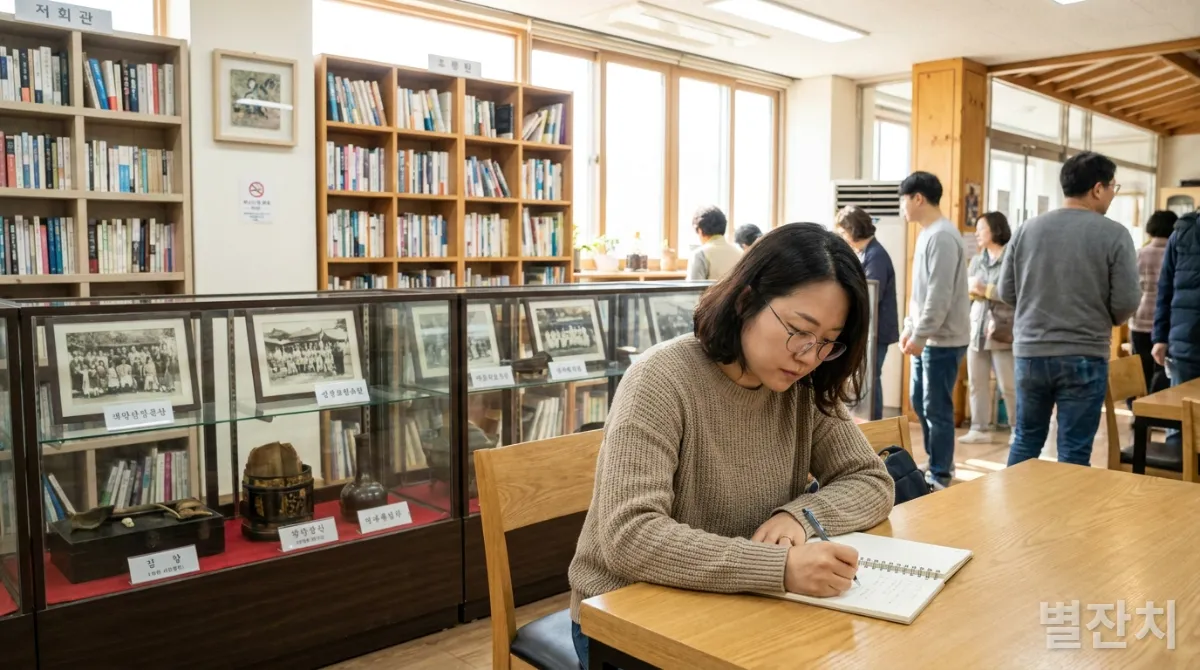 30대 한국인이 지역 커뮤니티 센터에서 공책에 필기하는 모습, 책장과 역사 전시물 배경