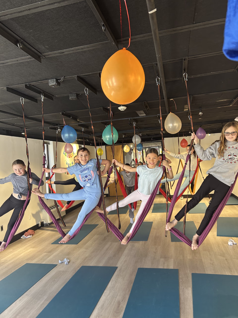 Kids posing in aerial hammocks with balloons hanging above them at a Yoga@Play birthday party