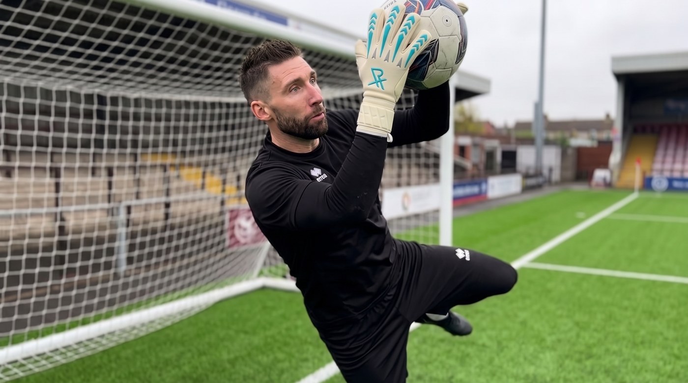 Goalkeeper catching a ball at full reach above head height in front of an empty goal