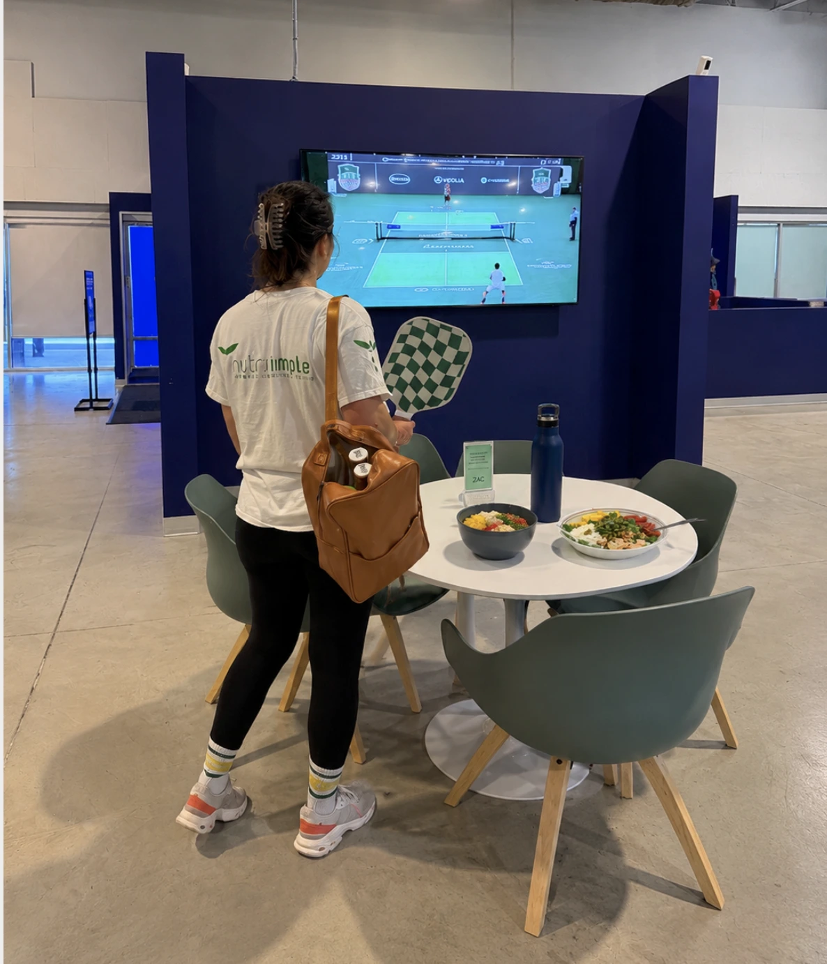 Bouteille d'eau et collation saine (fruits et noix) posées sur un banc à côté d'un terrain de pickleball, soulignant l'importance de l'hydratation et de l'énergie.