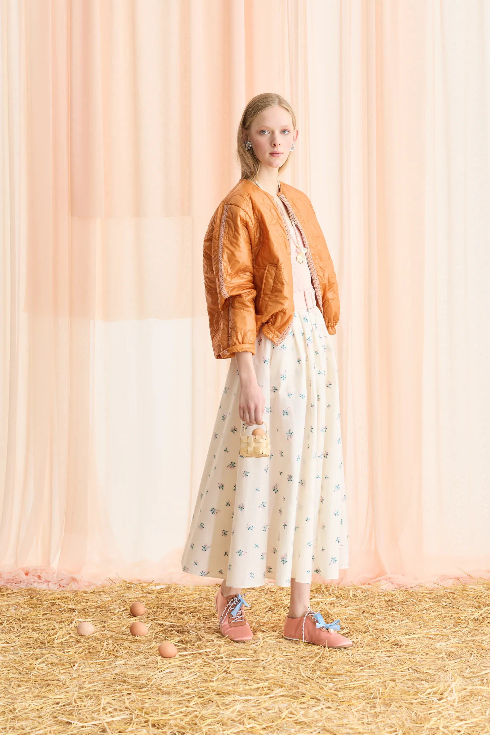 Modella con bomber arancio, gonna floreale e piccola borsa intrecciata nella collezione Forte_Forte Resort 2027
