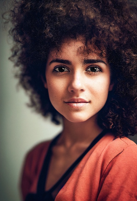 Portrait of a person with curly hair wearing a coral top, looking at the camera with a neutral expression