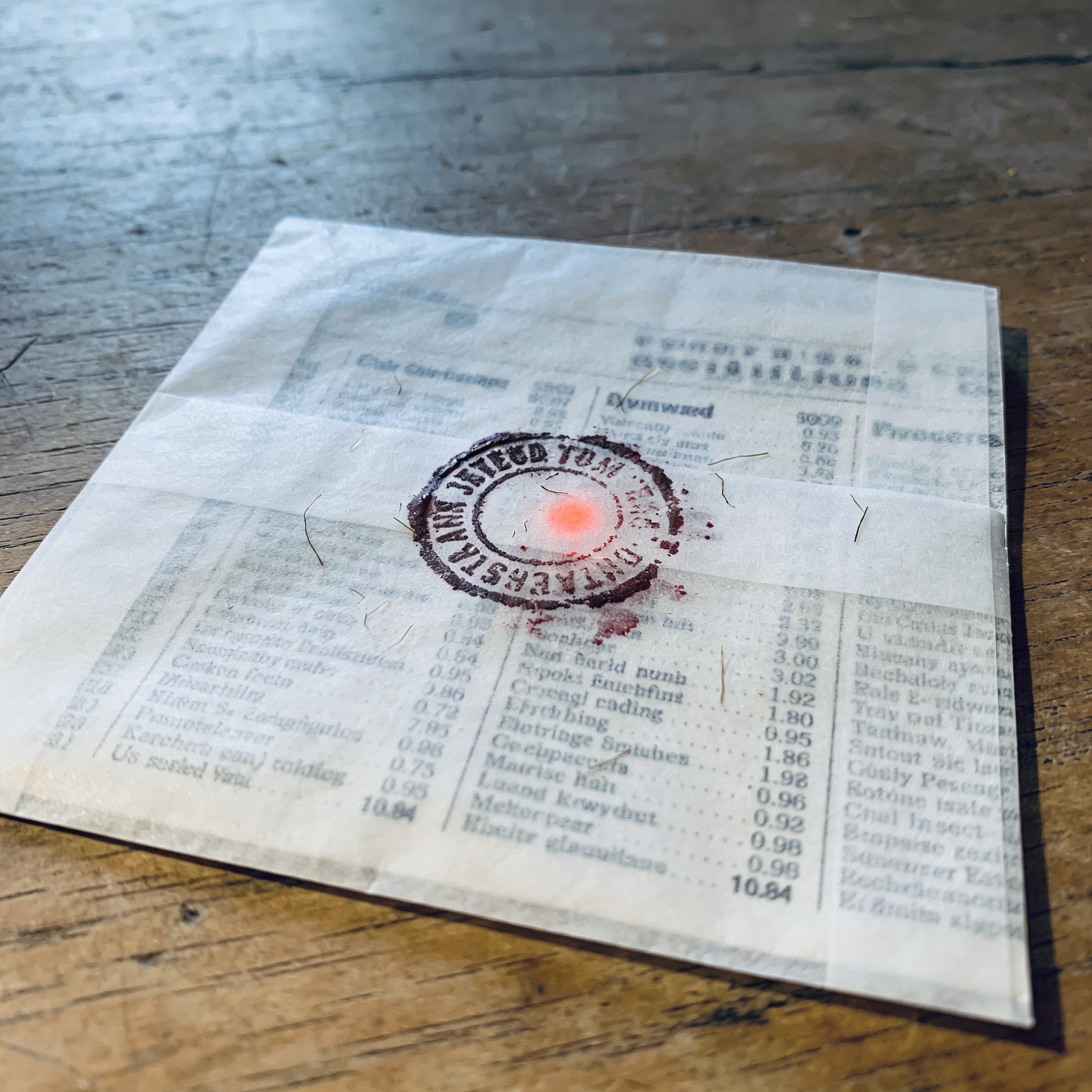 Smudged circular stamp on translucent paper over a blurred classified ad page.