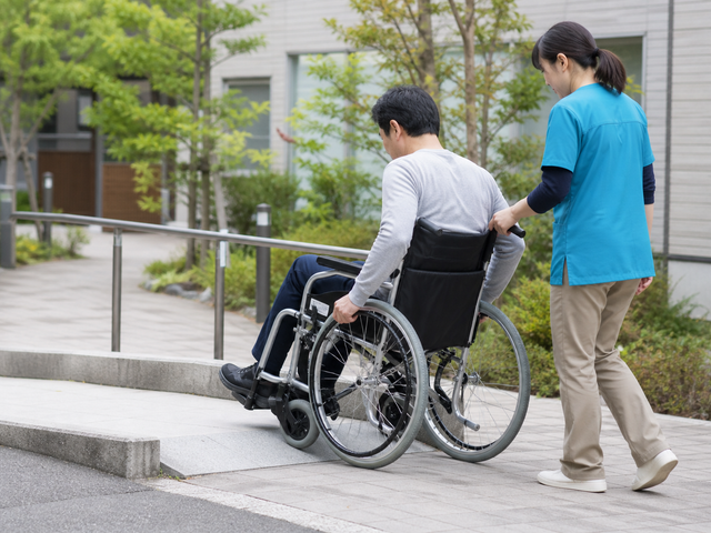 作業療法士の見守りのもとで屋外の段差とスロープを車椅子で練習する様子