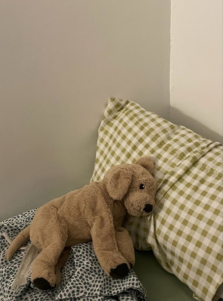 A photo of a dog plushie looking slightly sad where it's resting on a pillow.