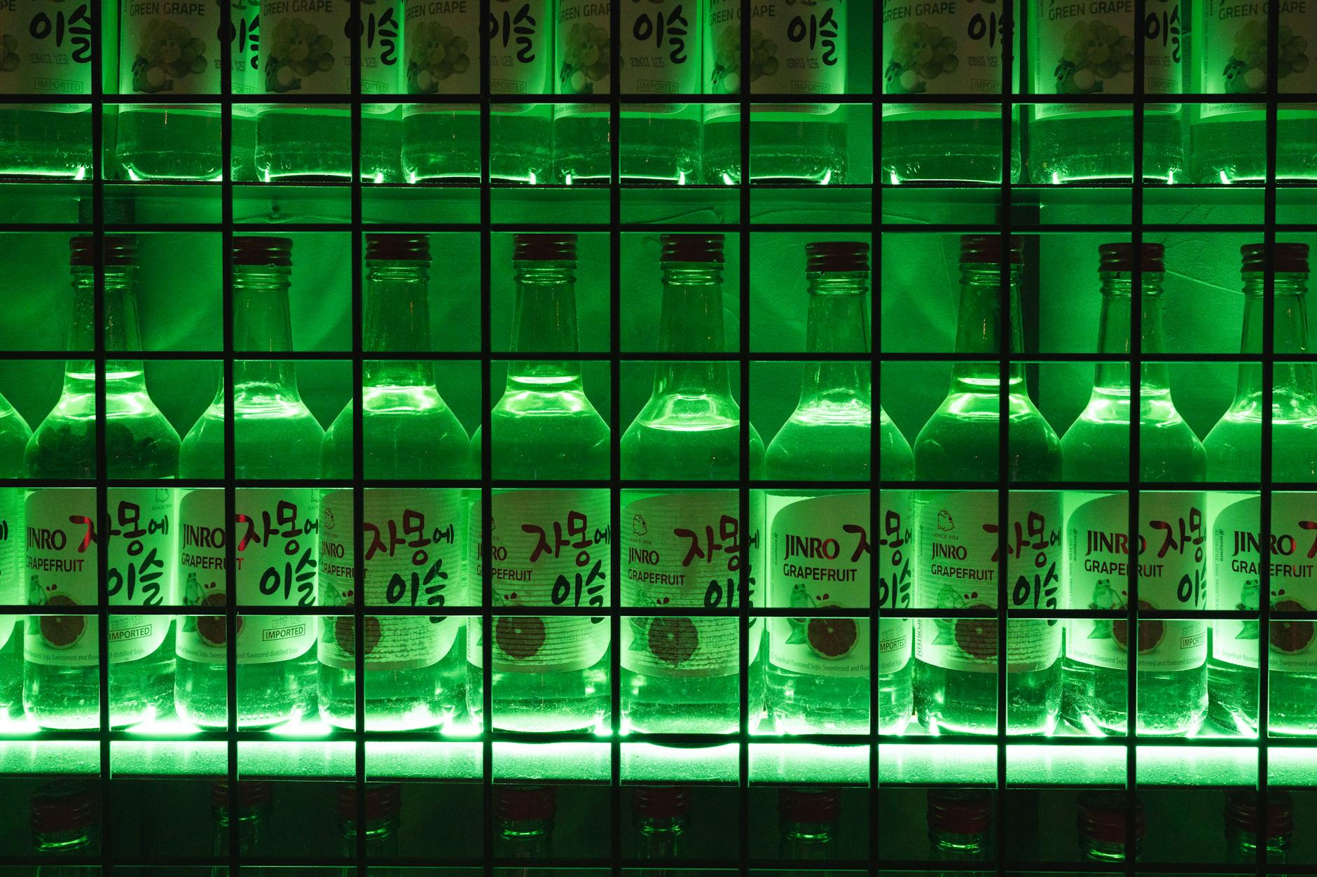 Illuminated Jinro flavored soju bottles displayed on a retail shelf, showing the iconic frog logo branding of Korea's best-selling soju brand