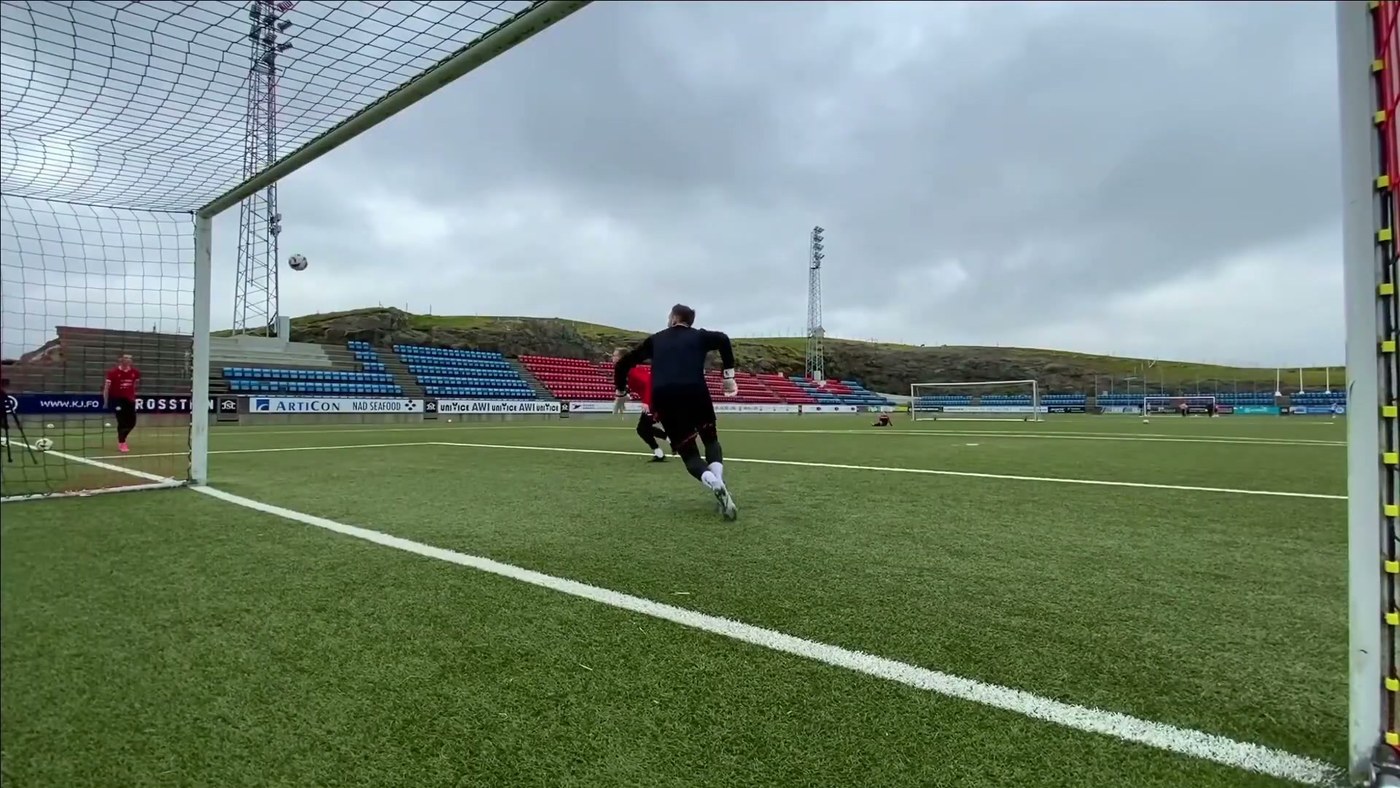 Goalkeeper seen from behind, sprinting out of his goal towards a cross in the air