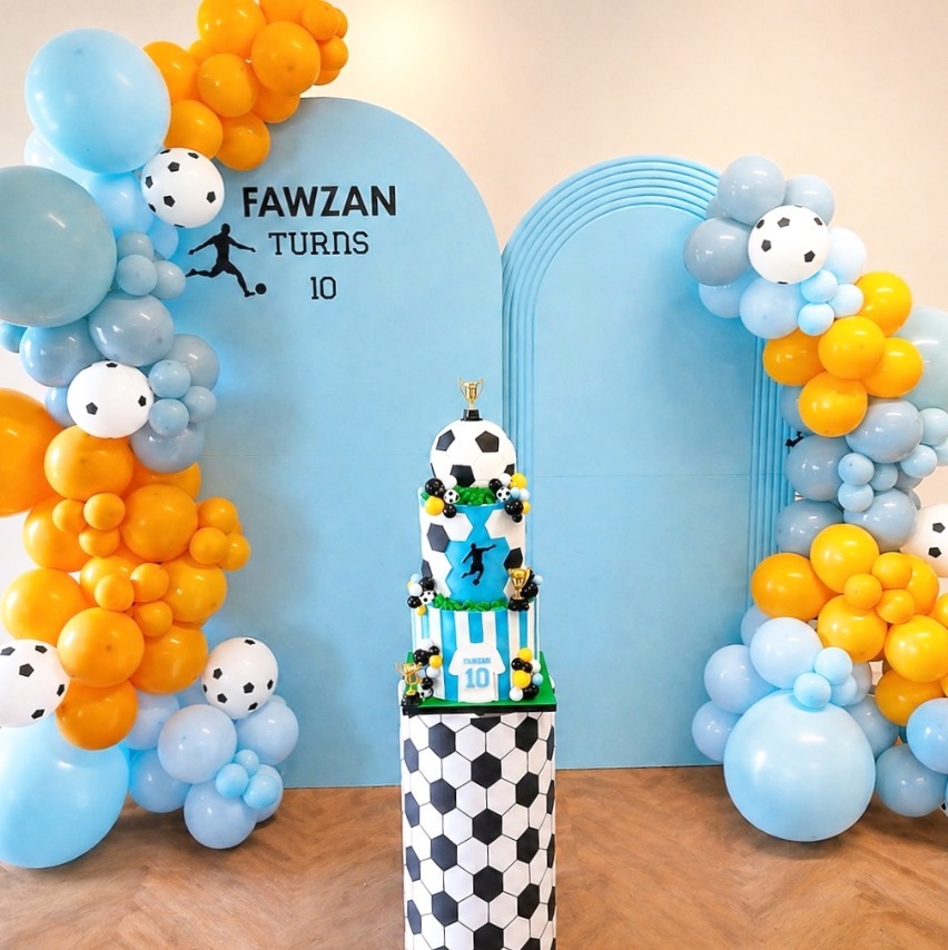 Soccer themed Fawzan Turns 10 light blue backdrop with soccer balloons and cake