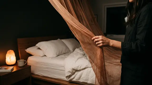 Hand pulling copper mesh bed canopy in dimly lit serene bedroom at night