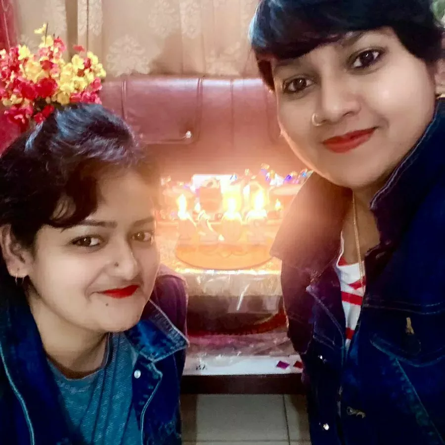 Elizabeth Two smiling women taking a selfie in front of a glowing birthday cake with lit candles.