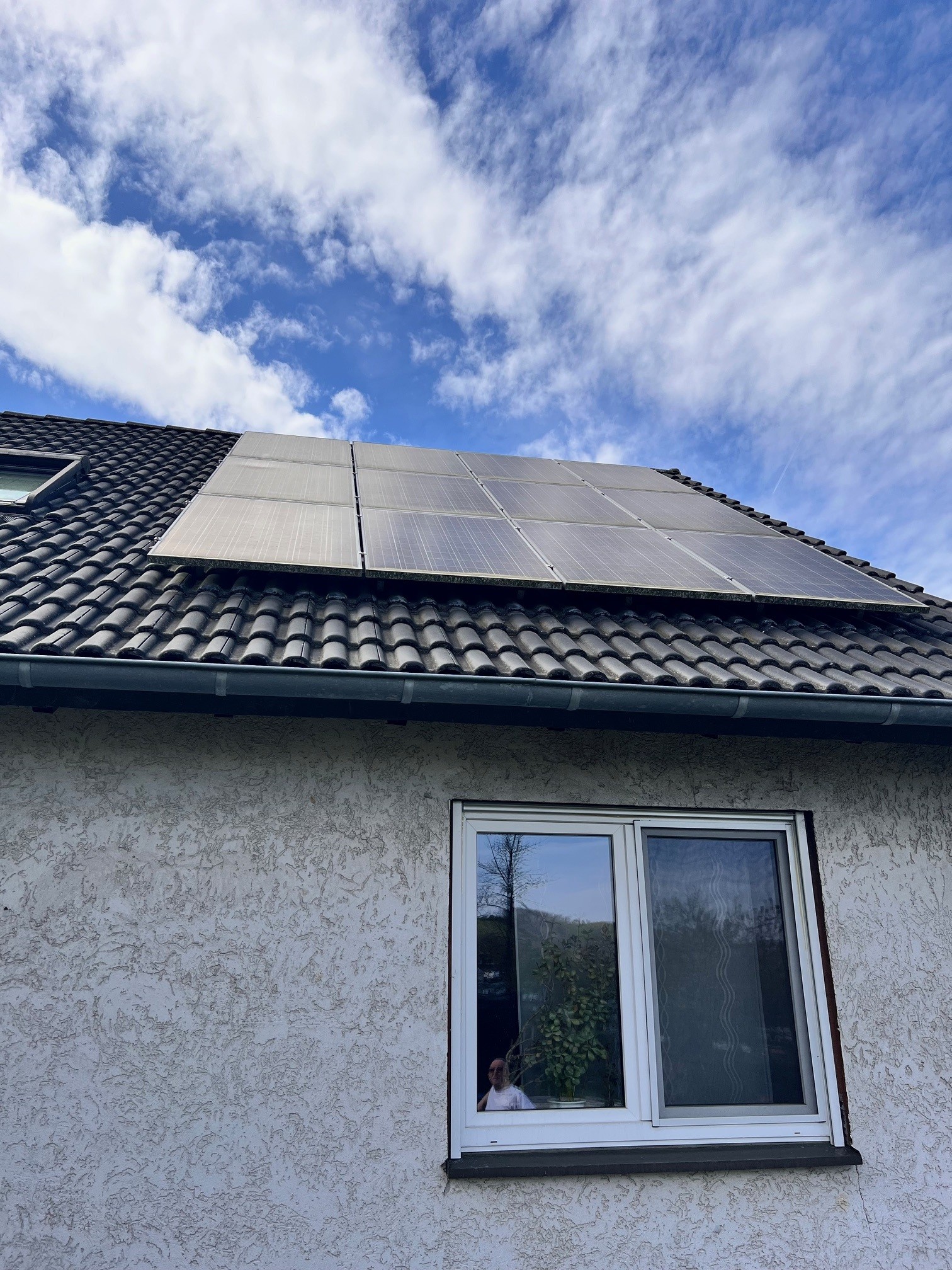 Privathaus mit PV-Anlage und Bewohner am Fenster