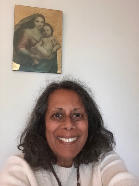 Smiling person taking a selfie indoors beneath a small framed portrait on a beige wall