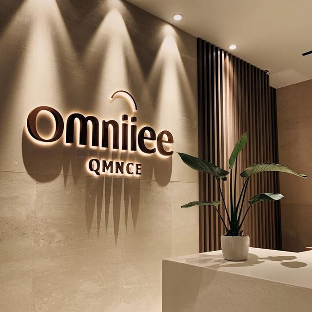 Custom face-lit acrylic script sign reading Studio T Transformation Awaits with decorative wood slat wall installation – signs.inc