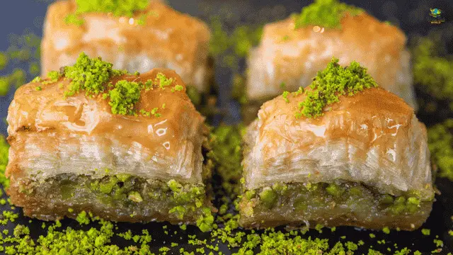 Greek baklava pieces layered with flaky phyllo pastry, pistachios, and honey syrup, garnished with crushed pistachios.