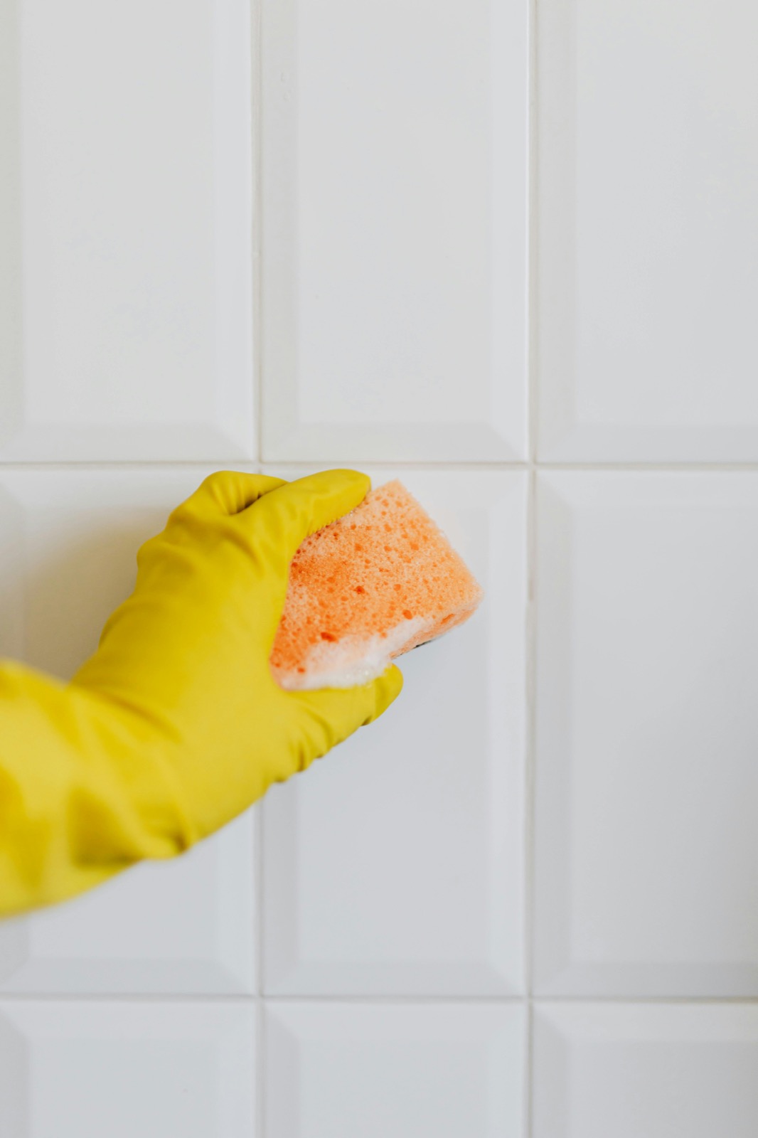 Gloved hand wiping bathroom tile with sponge