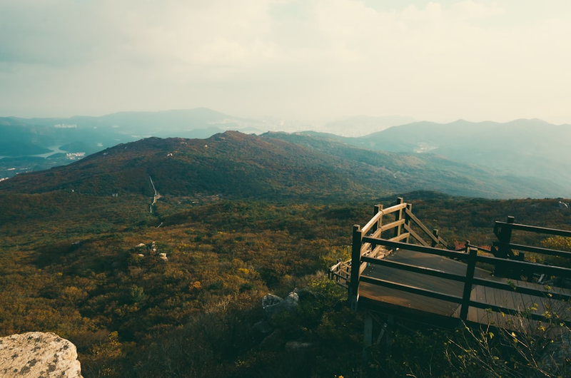 Wooden boardwalk railing on Hallasan mountain trail with panoramic views across Jeju Island's forested ridgeline and distant valleys on the Seongpanak hiking route