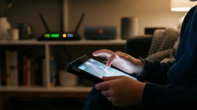 Child's small hands holding glowing tablet in dim room near Wi-Fi router, concerned mood