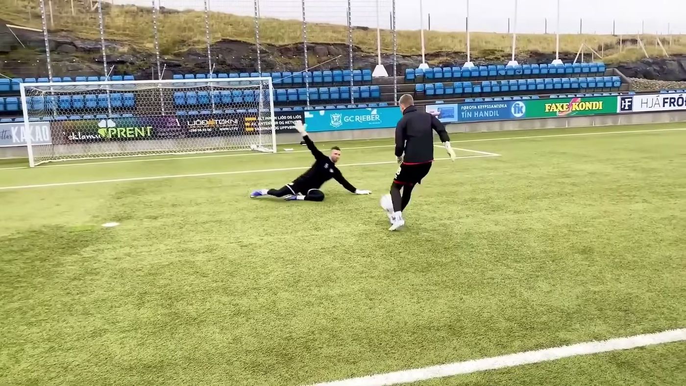 Goalkeeper diving low to his weaker side to reach a ball, body close to the ground
