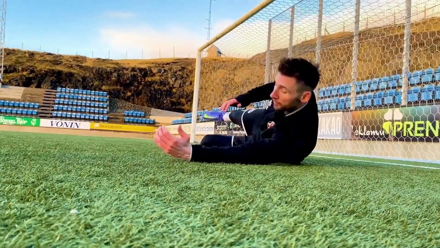 Goalkeeper sitting on the grass gliding sideways onto the ball with both hands