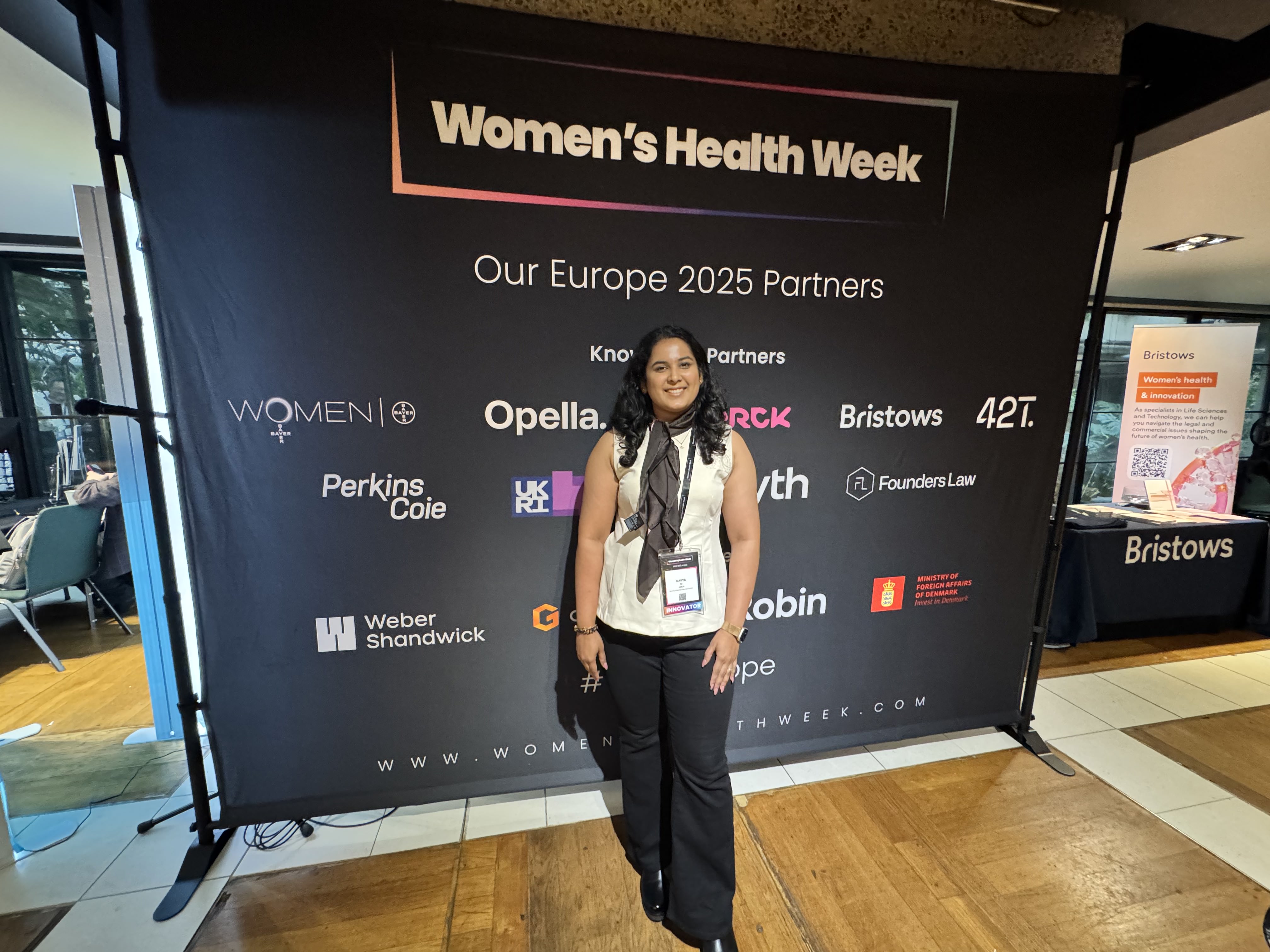 Navya Muralidhar at Women's Health Week, standing in front of the partners board.