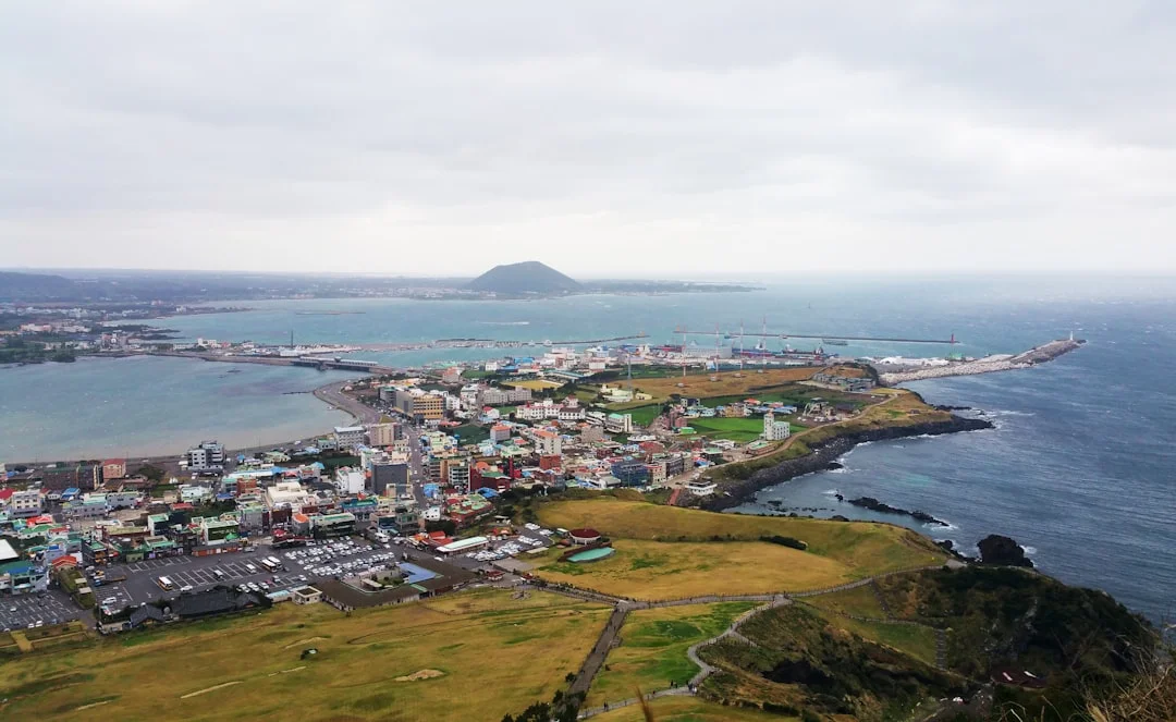 Seongsan Ilchulbong tuff cone rising from Jeju's eastern coast, grassy crater and turquoise ocean visible from the summit viewpoint