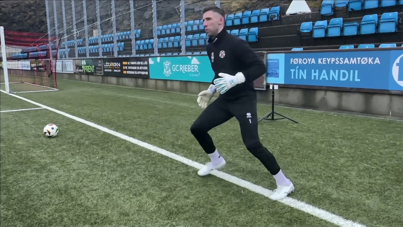 Goalkeeper shuffling sideways across the grass towards a ball on the ground