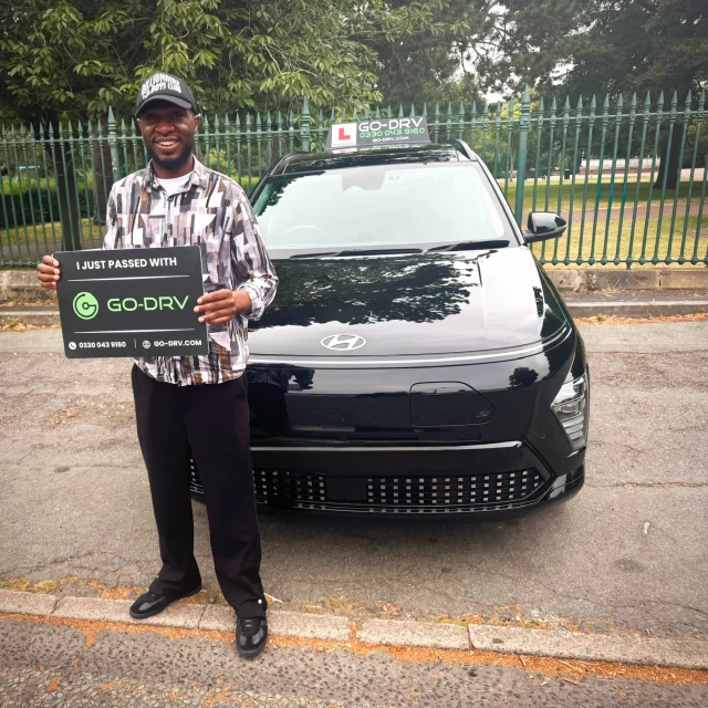 GO-DRV student Michael T. holding pass sign in front of black Hyundai Kona EV automatic tuition car in Wolverhampton