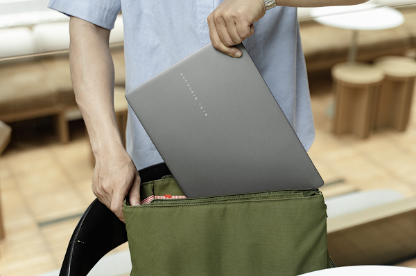 A person is holding a laptop with a green backpack next to them, seated at a table with a chair. AI-generated content may be incorrect.
