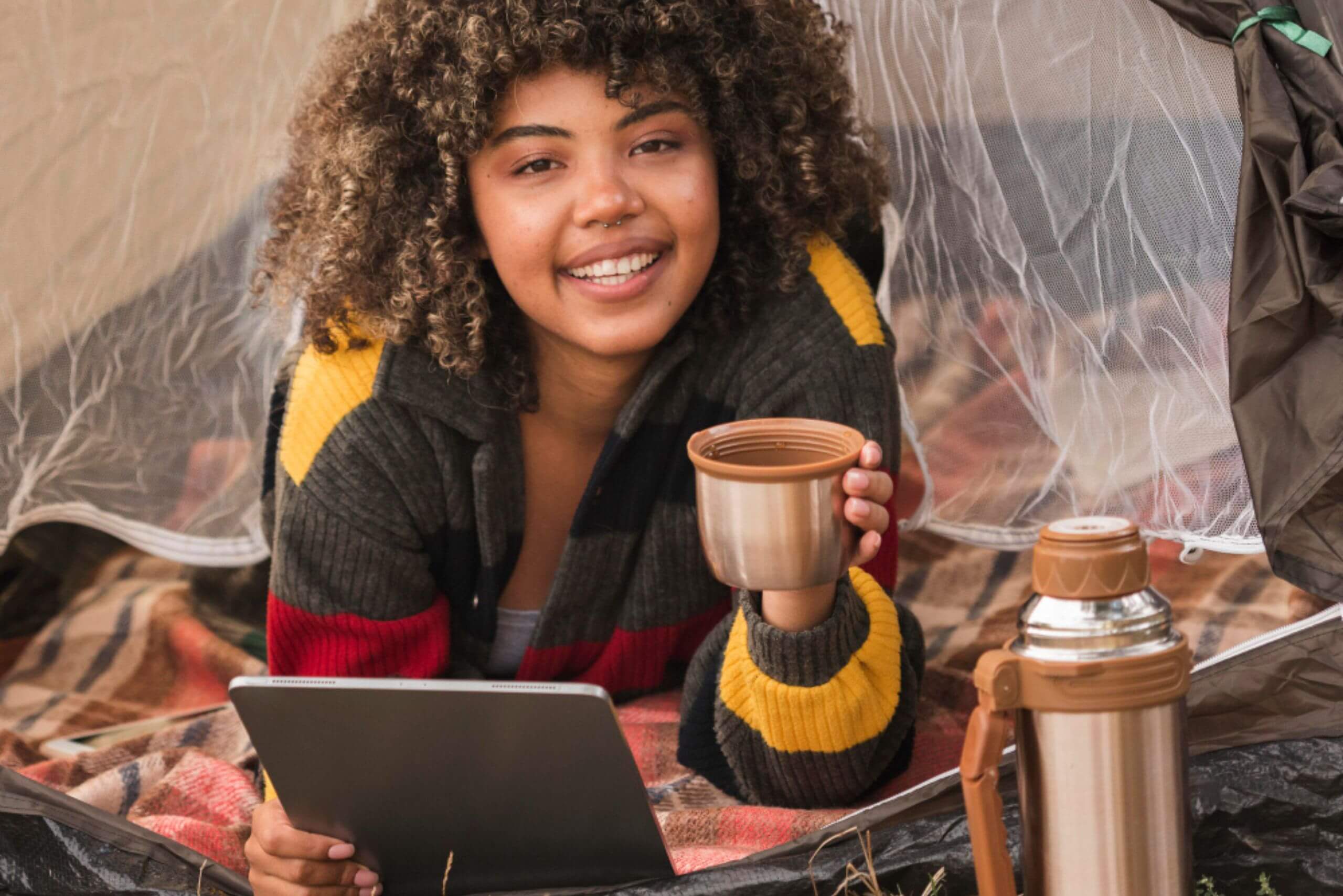 An image showing a lady relaxing while camping, using her tablet, portraying a digital nomad lifestyle.