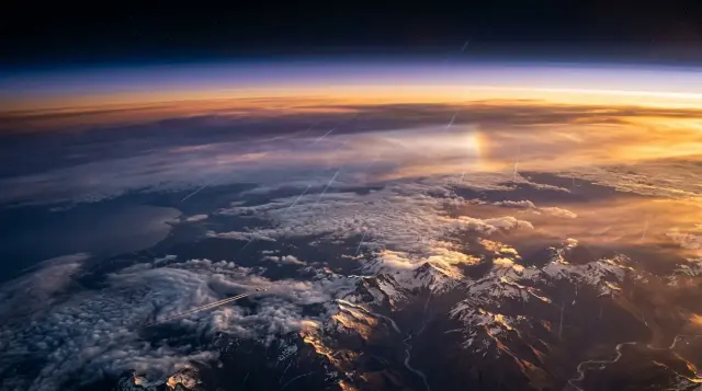 Luminous cosmic ray trails penetrating atmospheric layers above mountainous landscape at golden hour