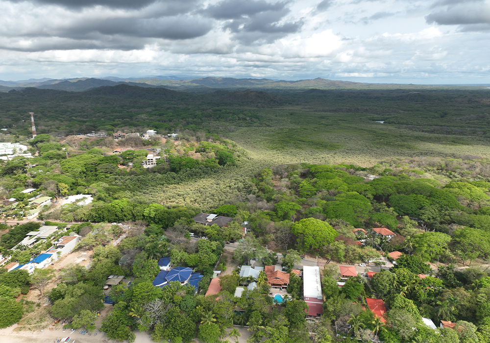 Aerial view of Tamarindo, Costa Rica, showcasing sandy beachfront and lush hillside landscape – ideal for international buyers choosing between coastal and elevated properties.